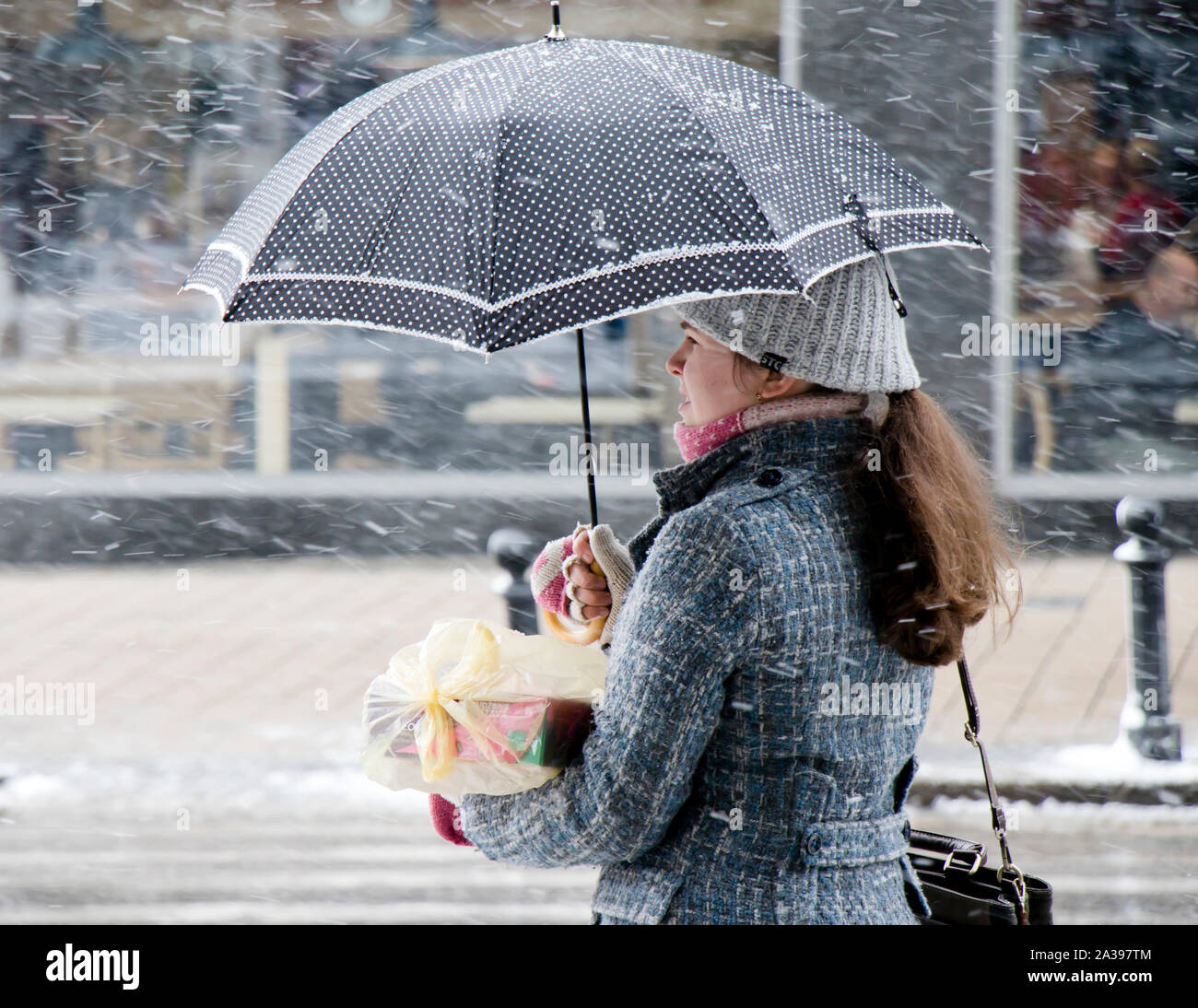Belgrade, Serbia - January 3, 2019: One young teenage girl standing alone under umbrella on snowy winter city street , waiting, in profile view Stock Photo