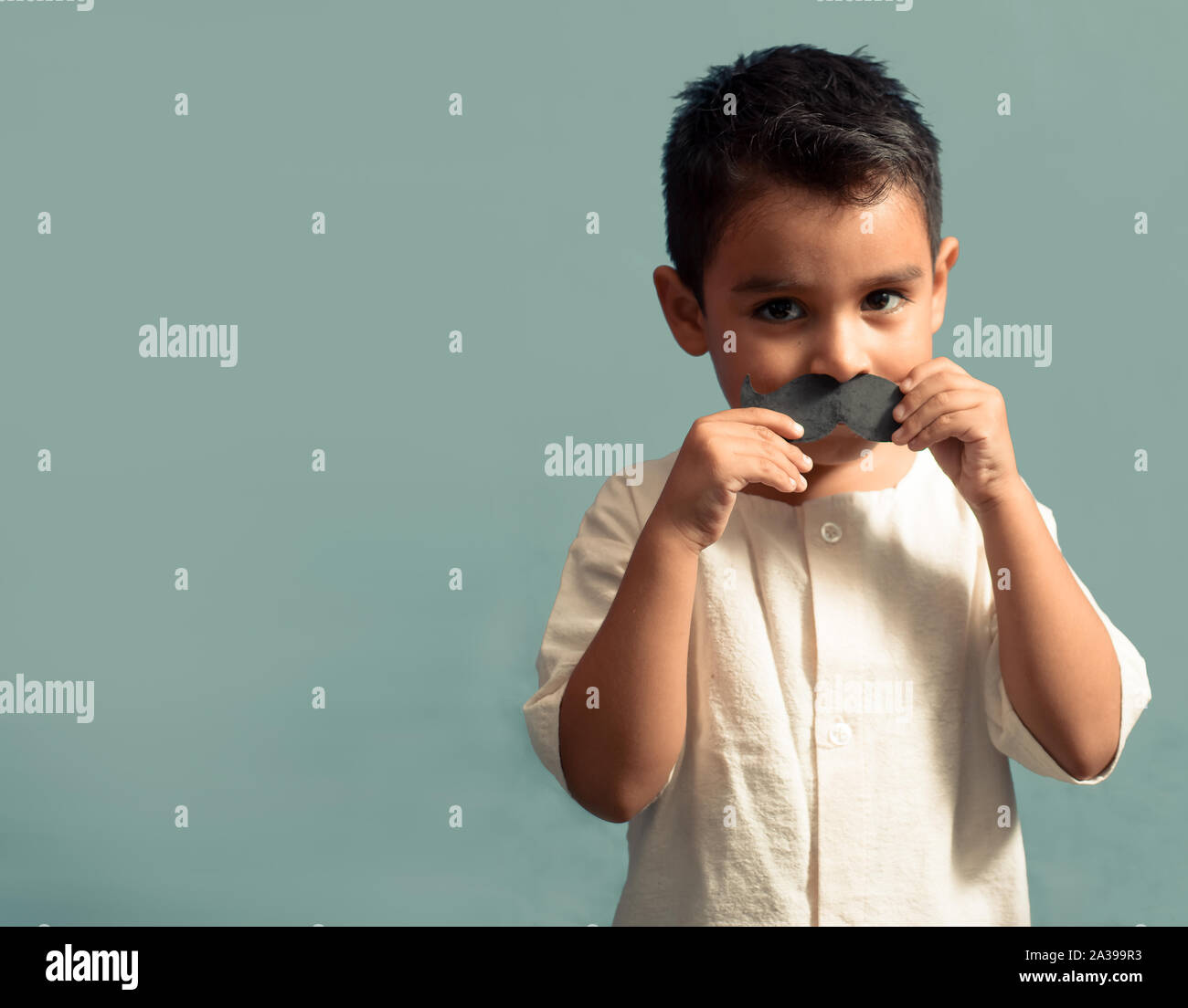 little kid joking with a fake paper moustache. Happy child playing in home. Isolated background. Movember concept. Stock Photo