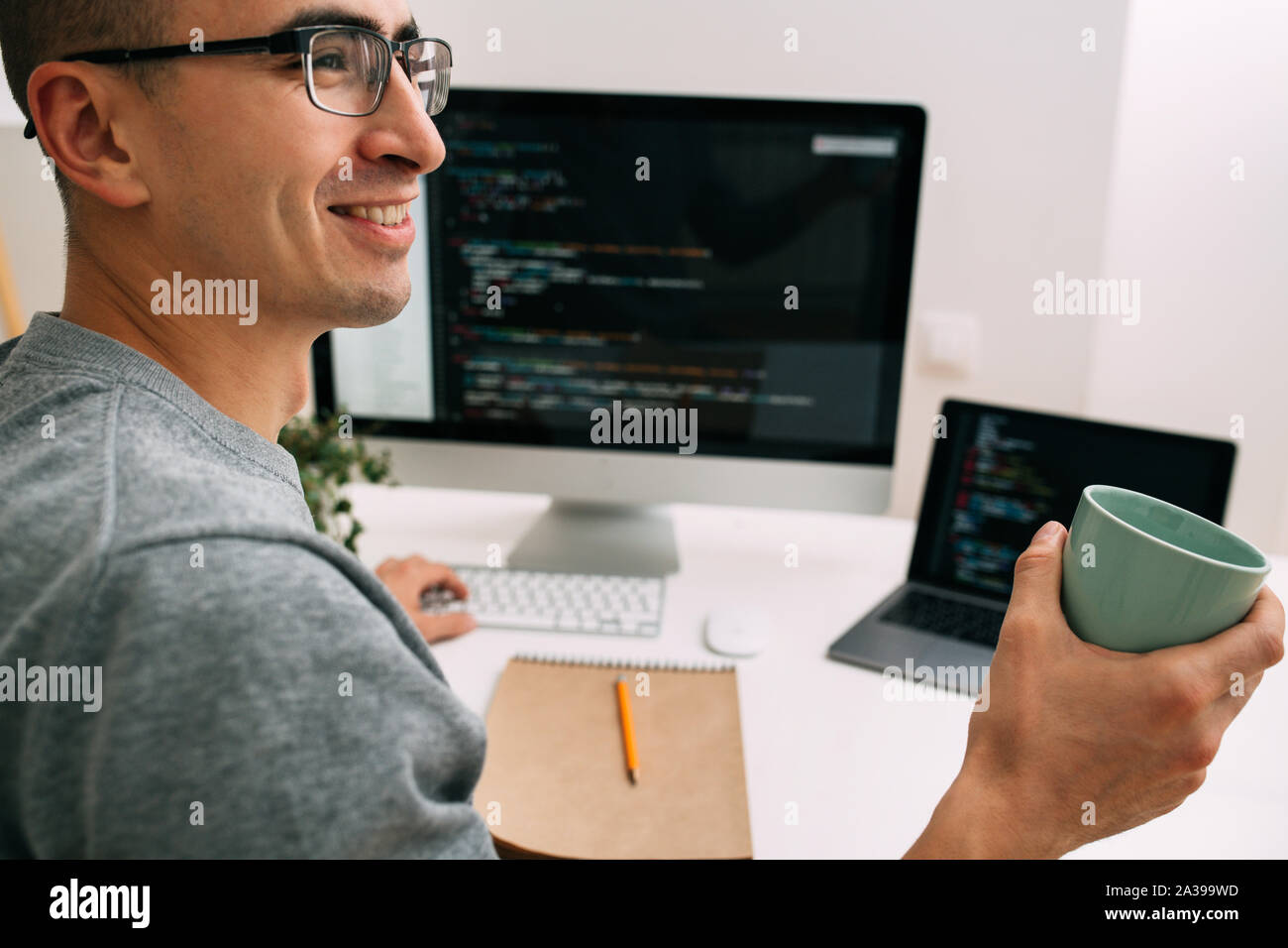 Programmer, working behind the desk, with two screens filled with code lines Stock Photo