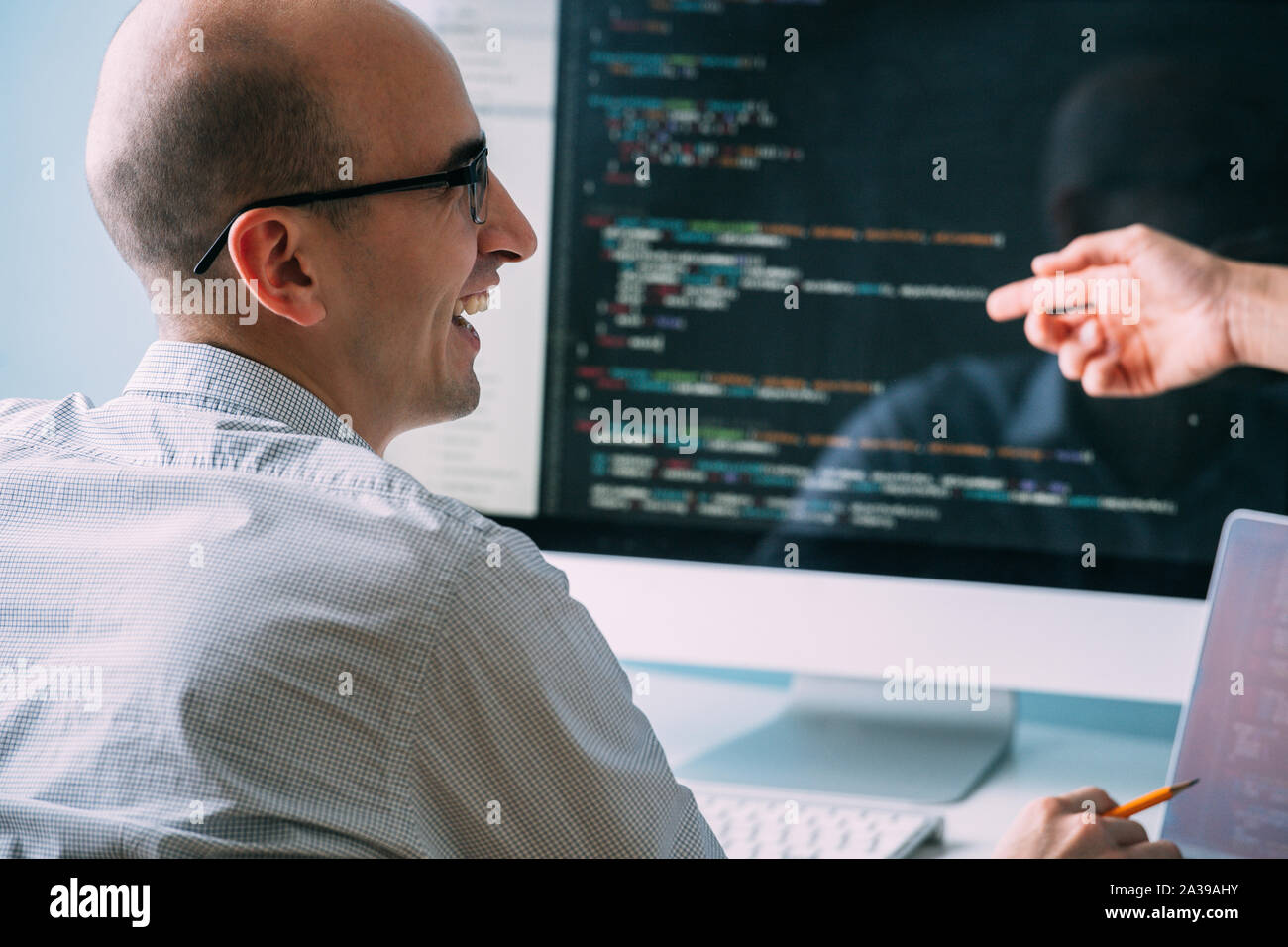 Programmer, working behind the desk, analysing code while chatting with coworker Stock Photo