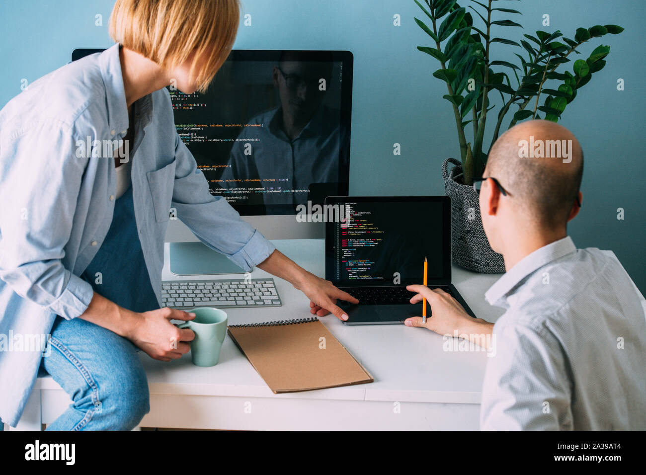 Programmer, working behind the desk, analysing code while chatting with coworker Stock Photo