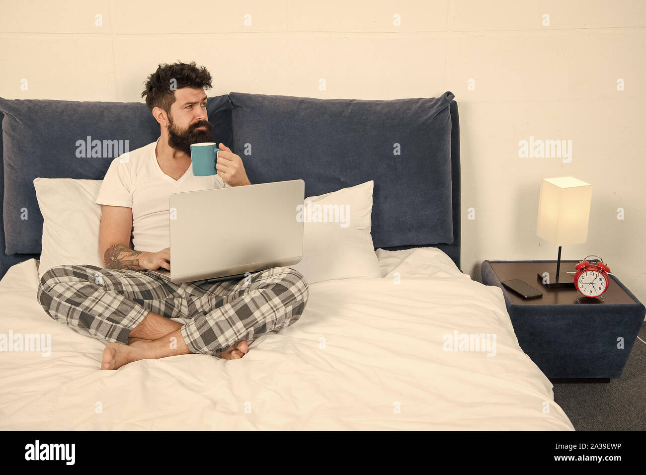 Hipster bearded guy pajamas freelance worker. Remote work concept. Social networks internet addiction. Online shopping. Man surfing internet or work online. Just woke up and already at work. Stock Photo