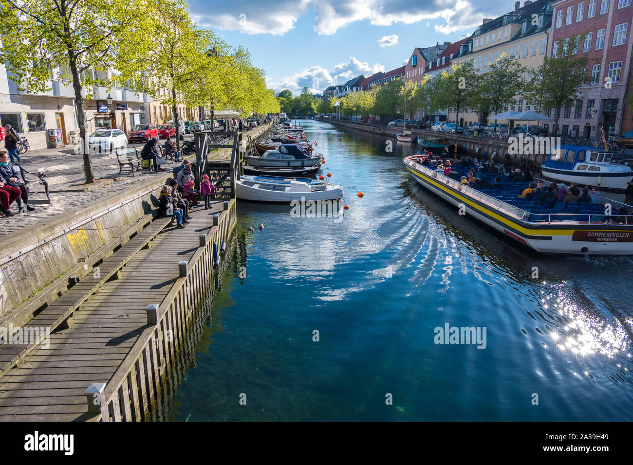 Copenhagen, Denmark - May 04, 2019: People relax on the waterfront while others explore Copenhagen on a tourist boat Stock Photo