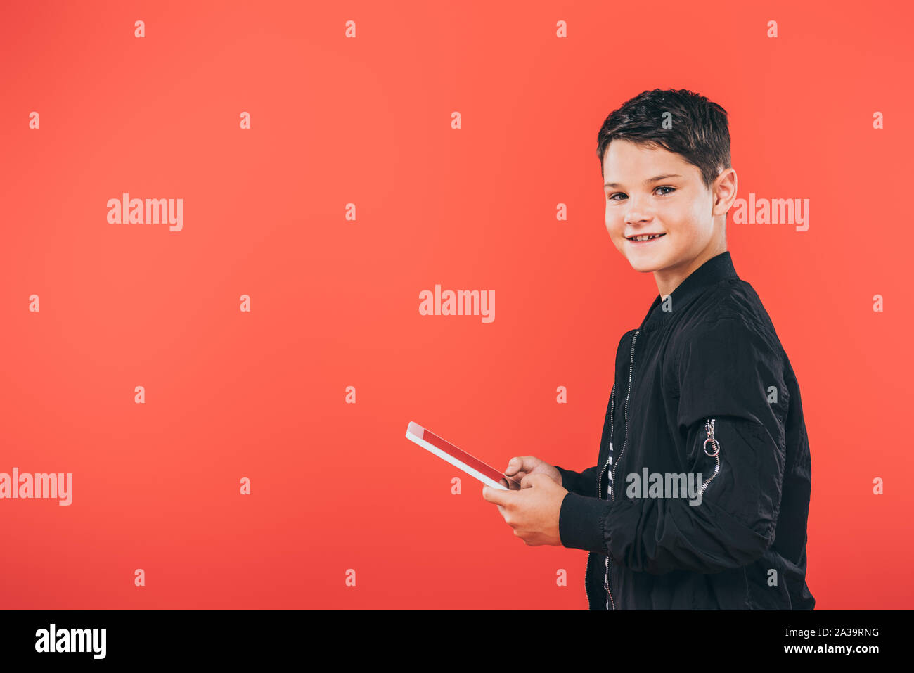 smiling kid in jacket using digital tablet isolated on red Stock Photo