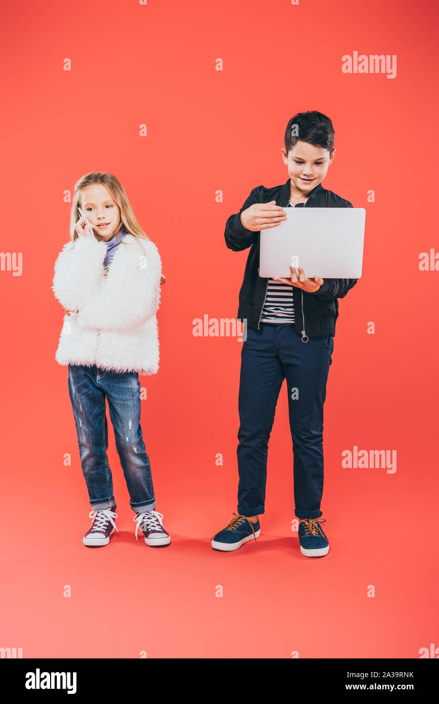 full length view of kids with smartphone and laptop on red Stock Photo