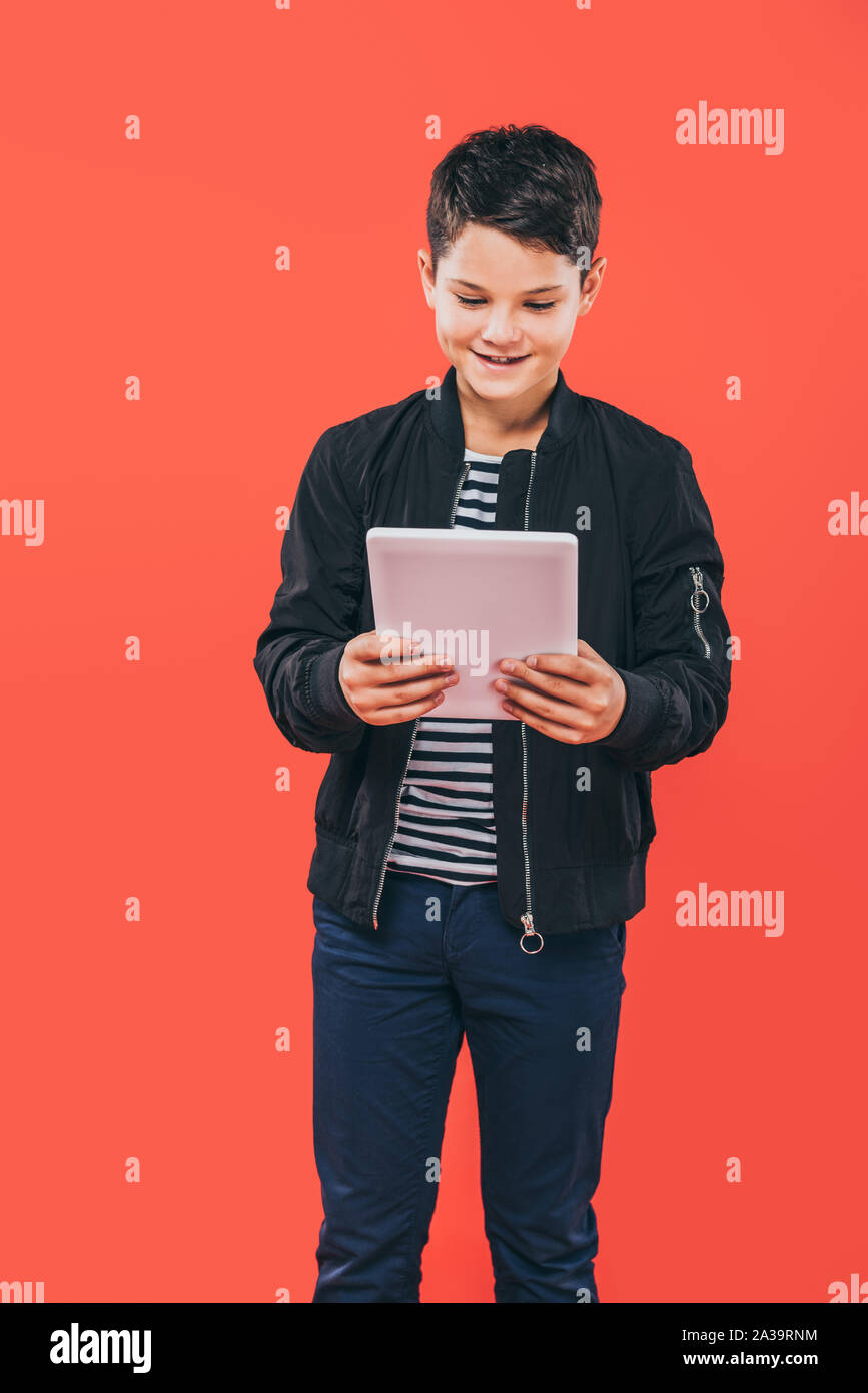smiling kid in jacket using digital tablet isolated on red Stock Photo