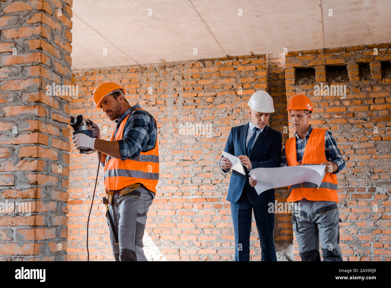 handsome builder using hammer drill near businessman and coworker Stock Photo
