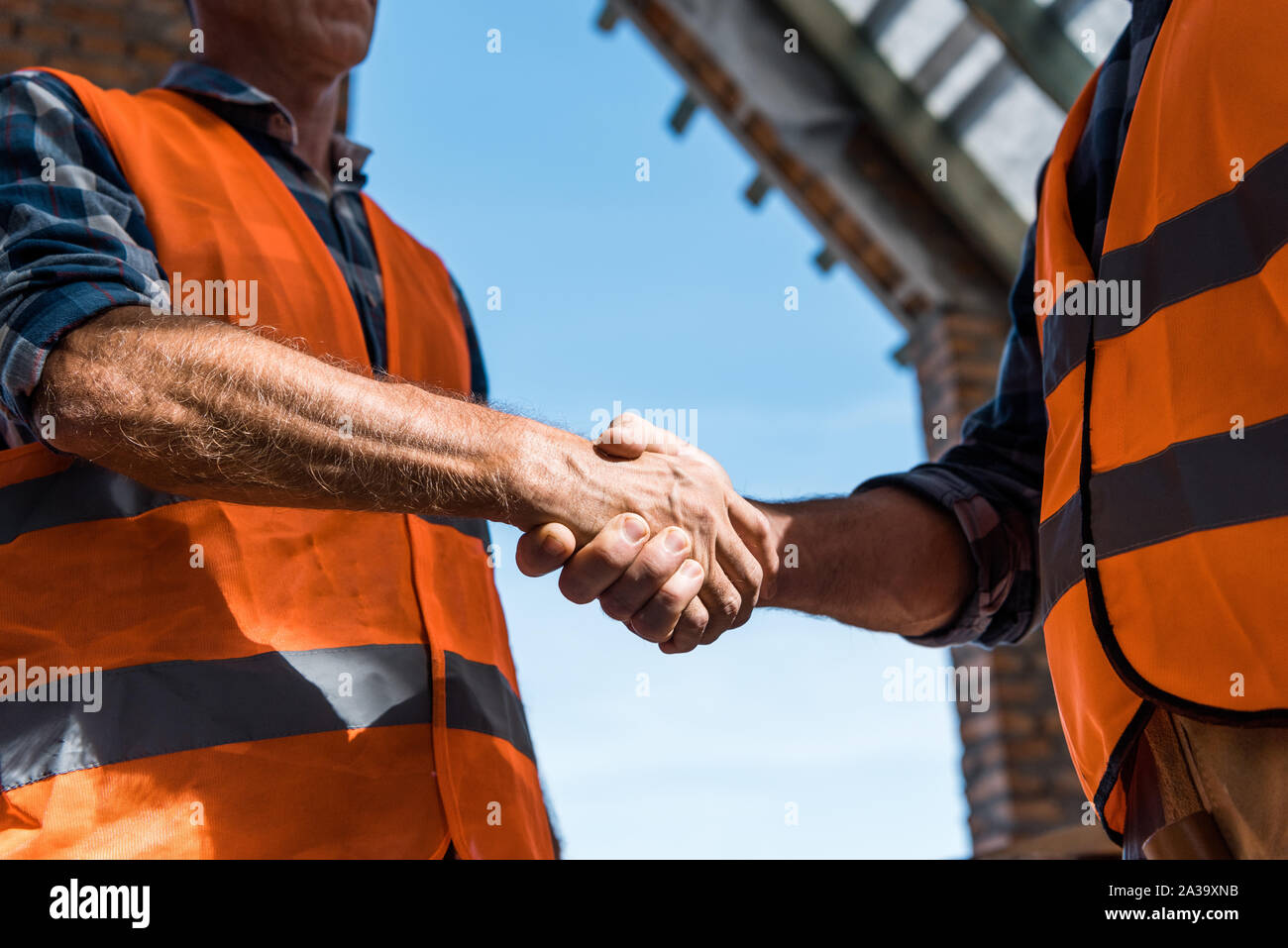cropped view of men shaking hands against blue sky Stock Photo