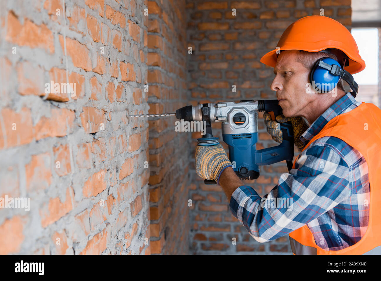 mature builder using hammer drill near brick wall Stock Photo