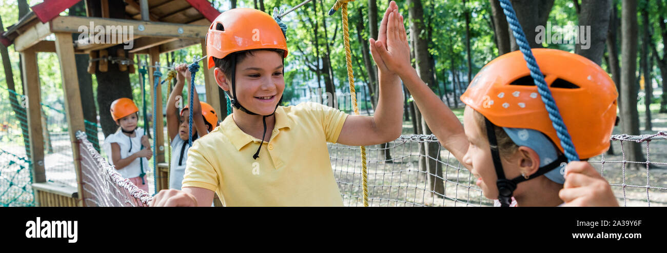 panoramic shot of smiling kids giving high five near multicultural fiends Stock Photo