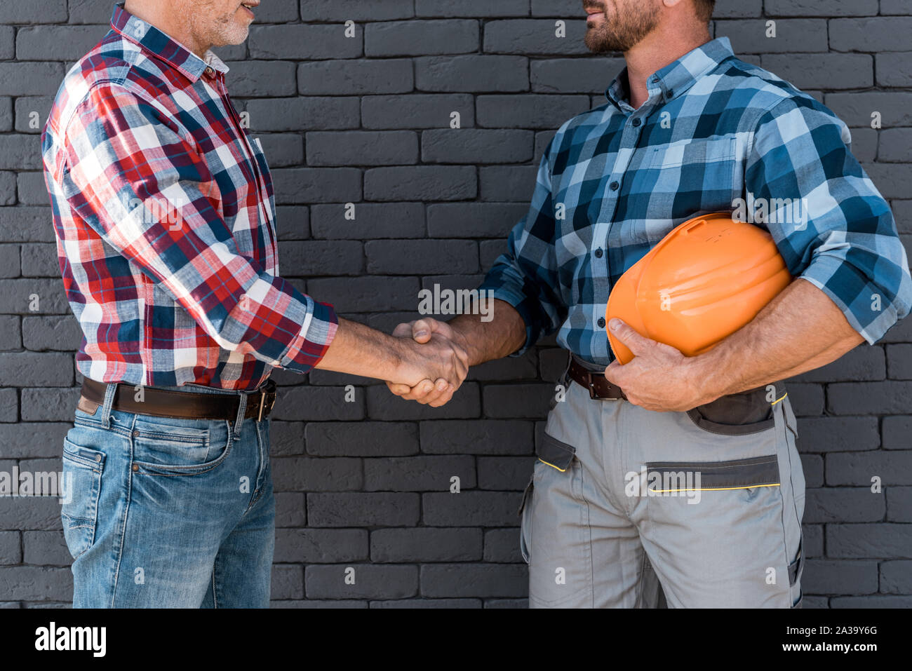 cropped view of men shaking hands while standing near brick wall Stock Photo