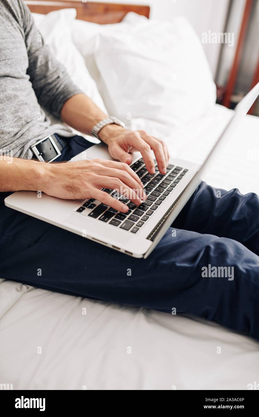 Cropped image of coding young man sitting on bed. Programmer working from home Stock Photo