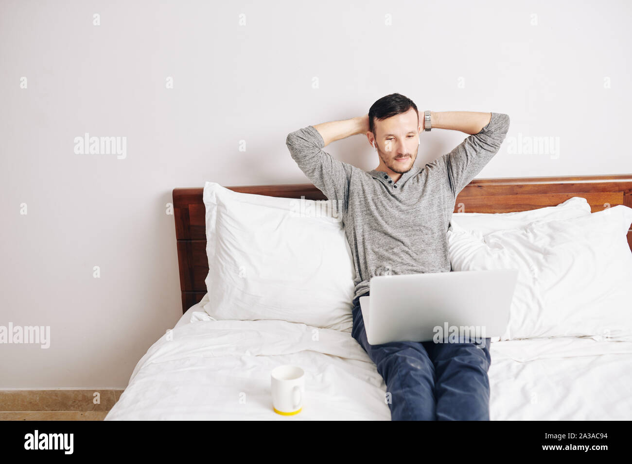 Handsome bearded man leaning back in his bed when watching new episode of popular show online Stock Photo