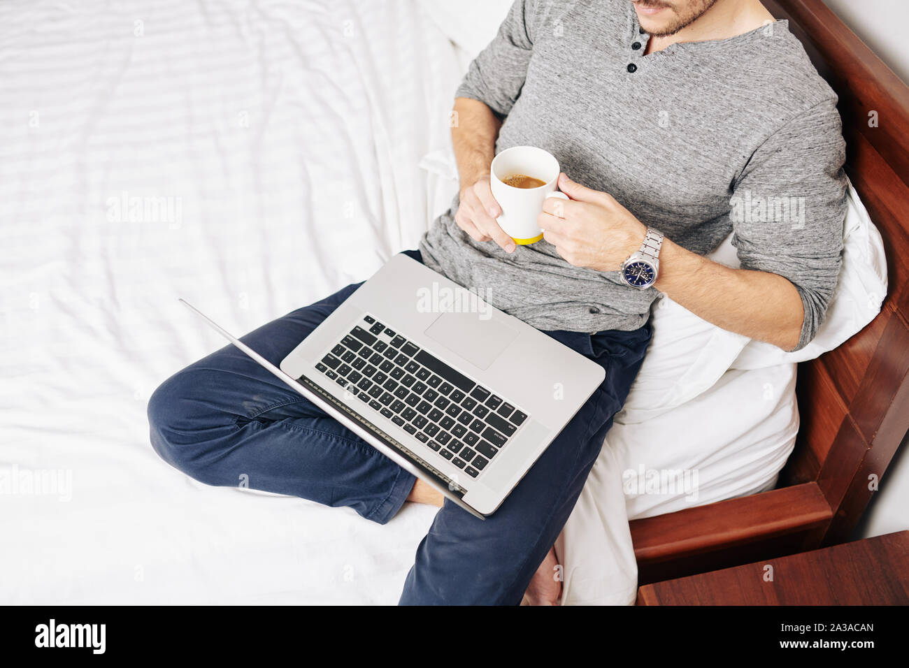 man leaning on big comfy chair on his bed drinking cup of
