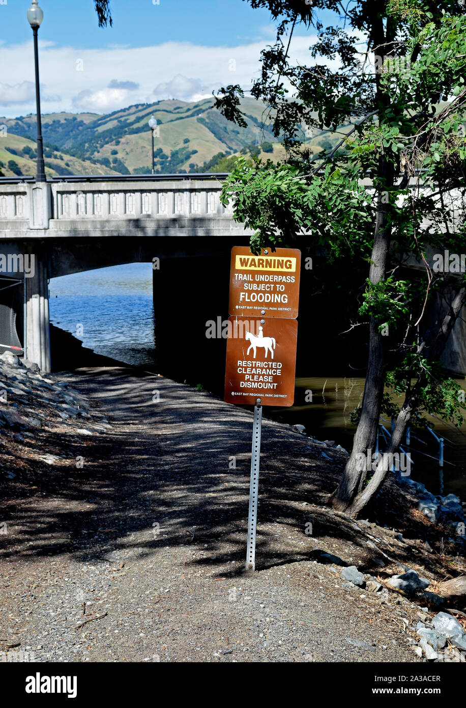 Restricted clearance Please dismount and warning, trail underpass subject to flooding sign near Mission Boulevard, Alameda Creek, Alameda County, California Stock Photo