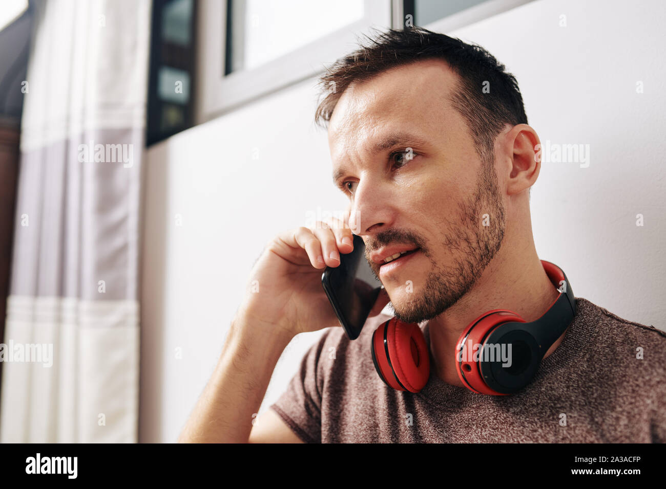 Serious Caucasian young man with headphones around his neck answering