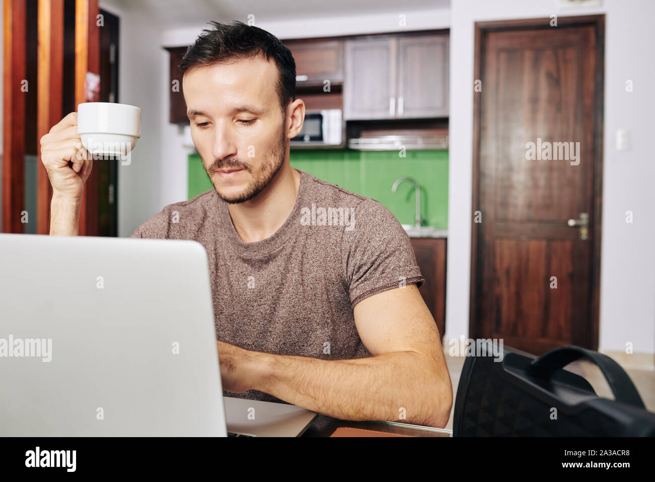 Bearden pensive man drinking cup of coffee and looking at programming code on laptop screen Stock Photo