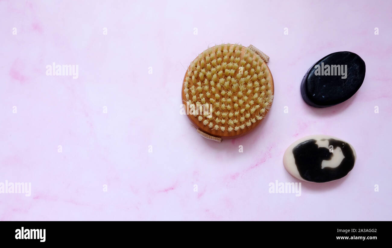 A round body scrub brush with two bars of black charcoal and milk body soap, on pink surface. Stock Photo
