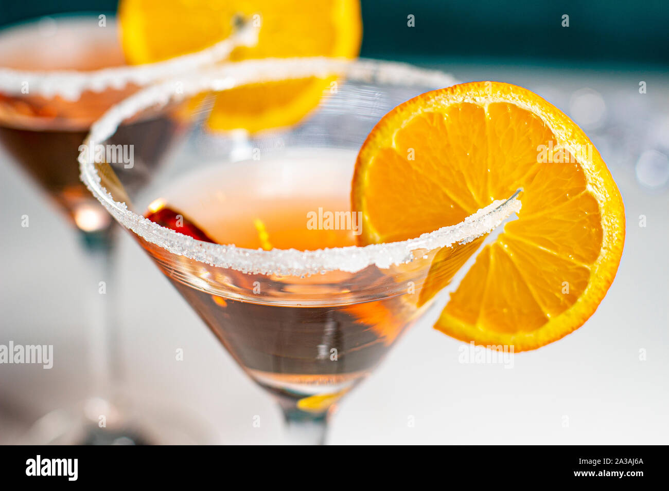 Top view of a cocktail with orange garnish with a green wooden wall and white table Stock Photo