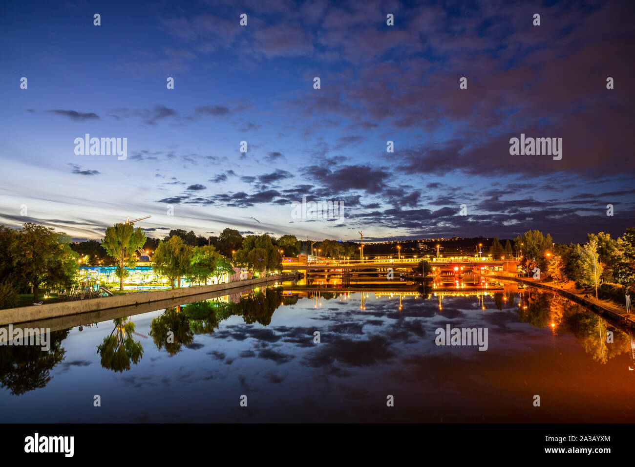 Germany, Scenic view over glassy neckar river reflecting tram and train driving by swimming pool of stuttgart bad canstatt by night in beautiful atmos Stock Photo