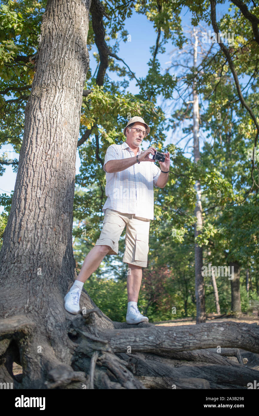 Mature man wearing hat holding photo camera while taking picture Stock Photo