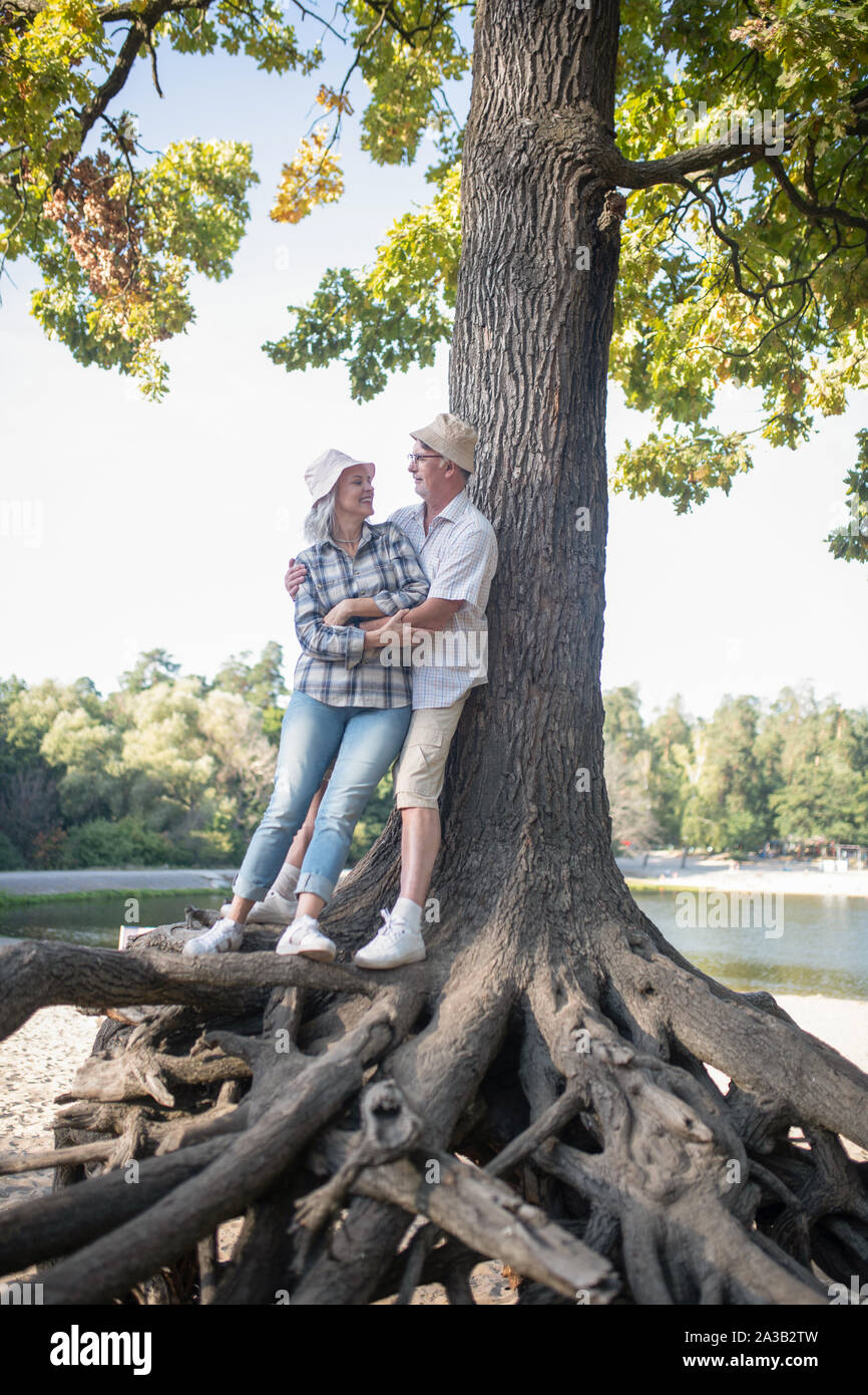 Couple of mature adults standing on roots of huge tree Stock Photo