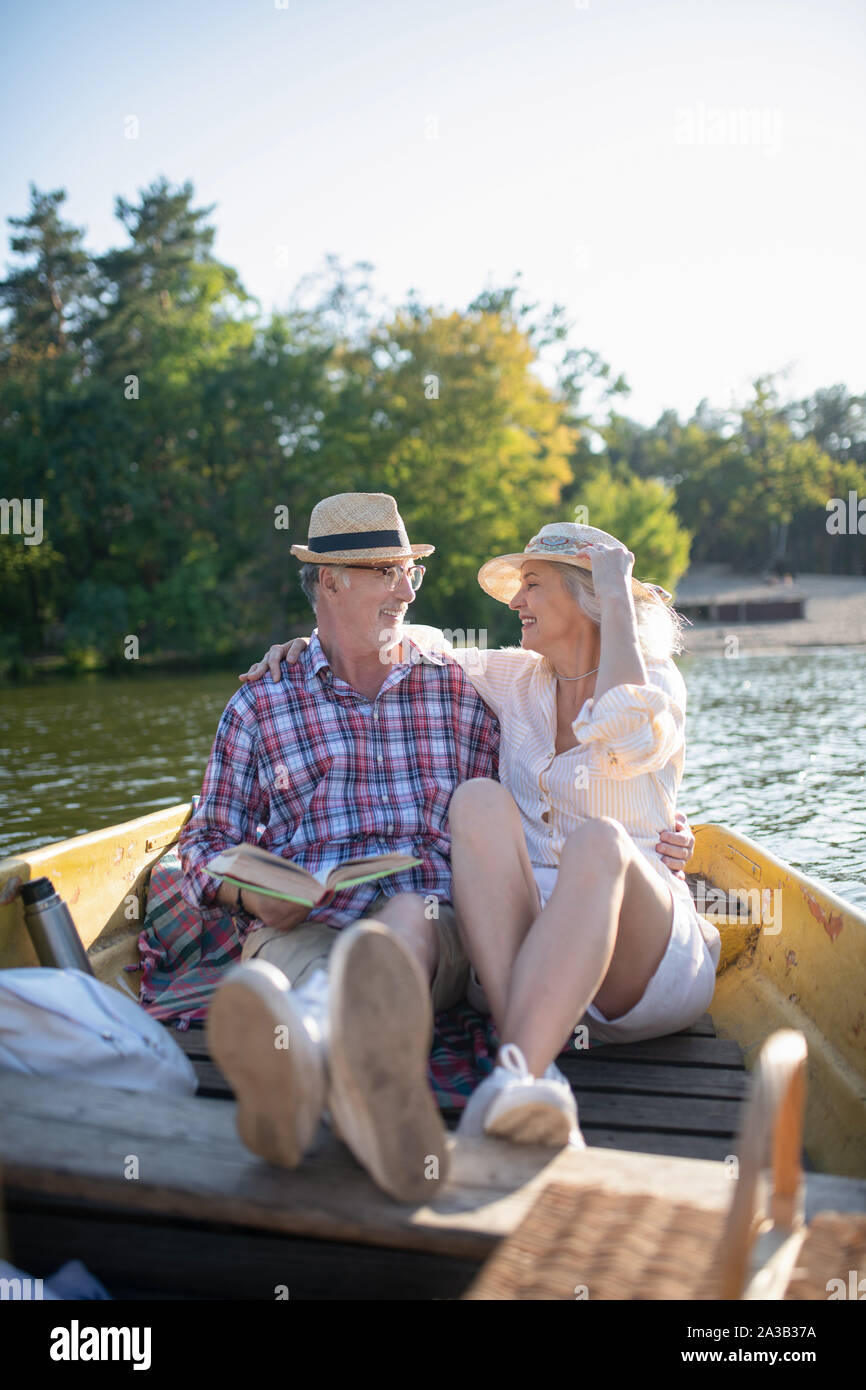 Senior adults sitting in boat and reading book while enjoying evening Stock Photo