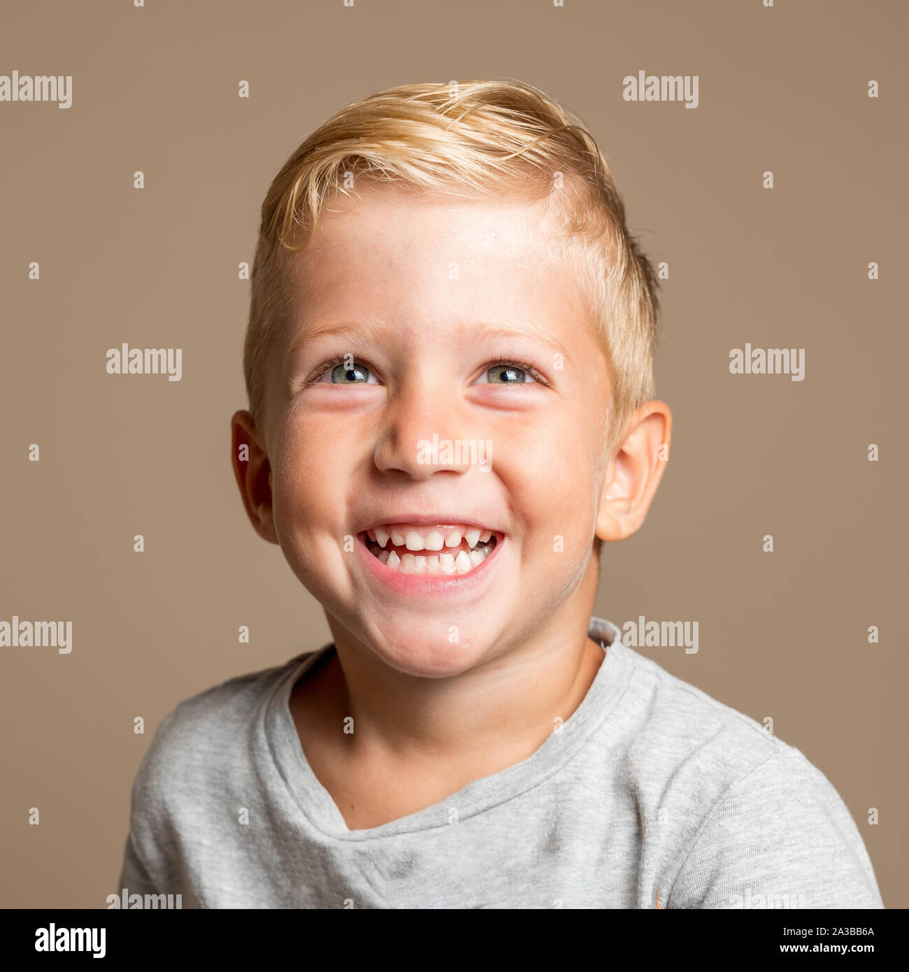 Close up of Baby boy smiling three year old, blond with green eyes on a light brown background, conceptual photo for dental hygiene and personal care. Stock Photo