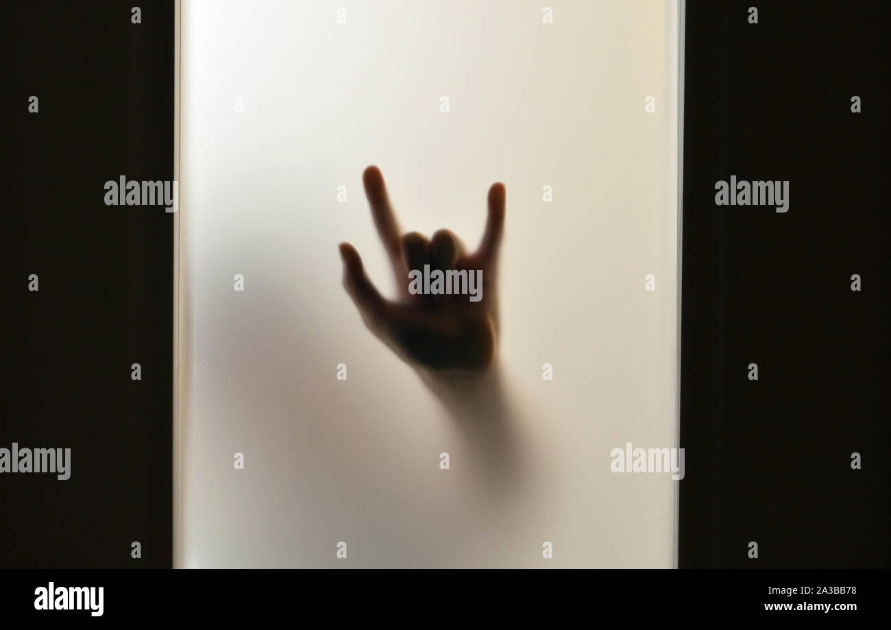Hand showing devil's horns through frosted glass Stock Photo