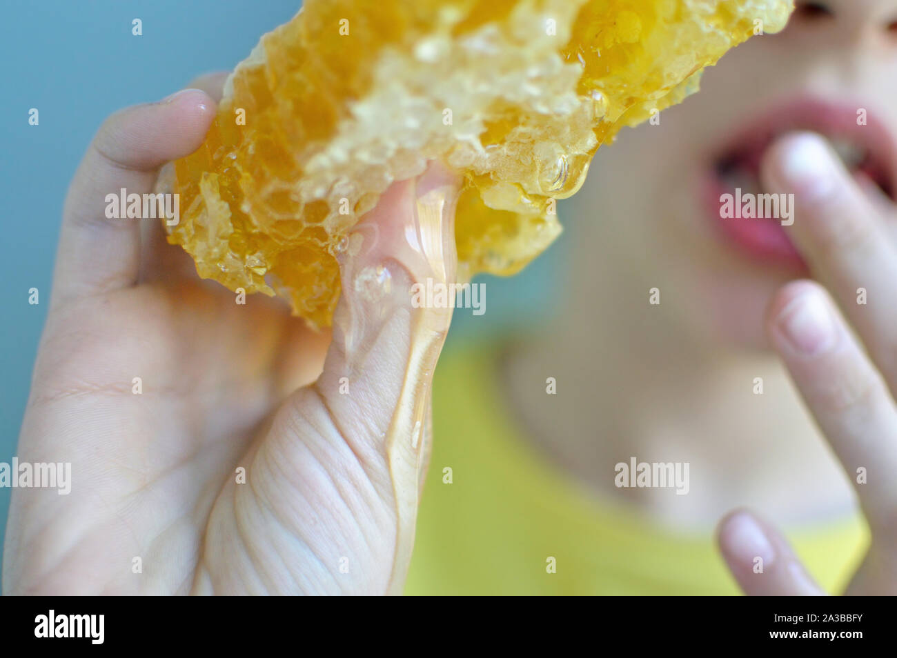 Close up shot of honeycomb and honey dripping with blurry girl in background Stock Photo