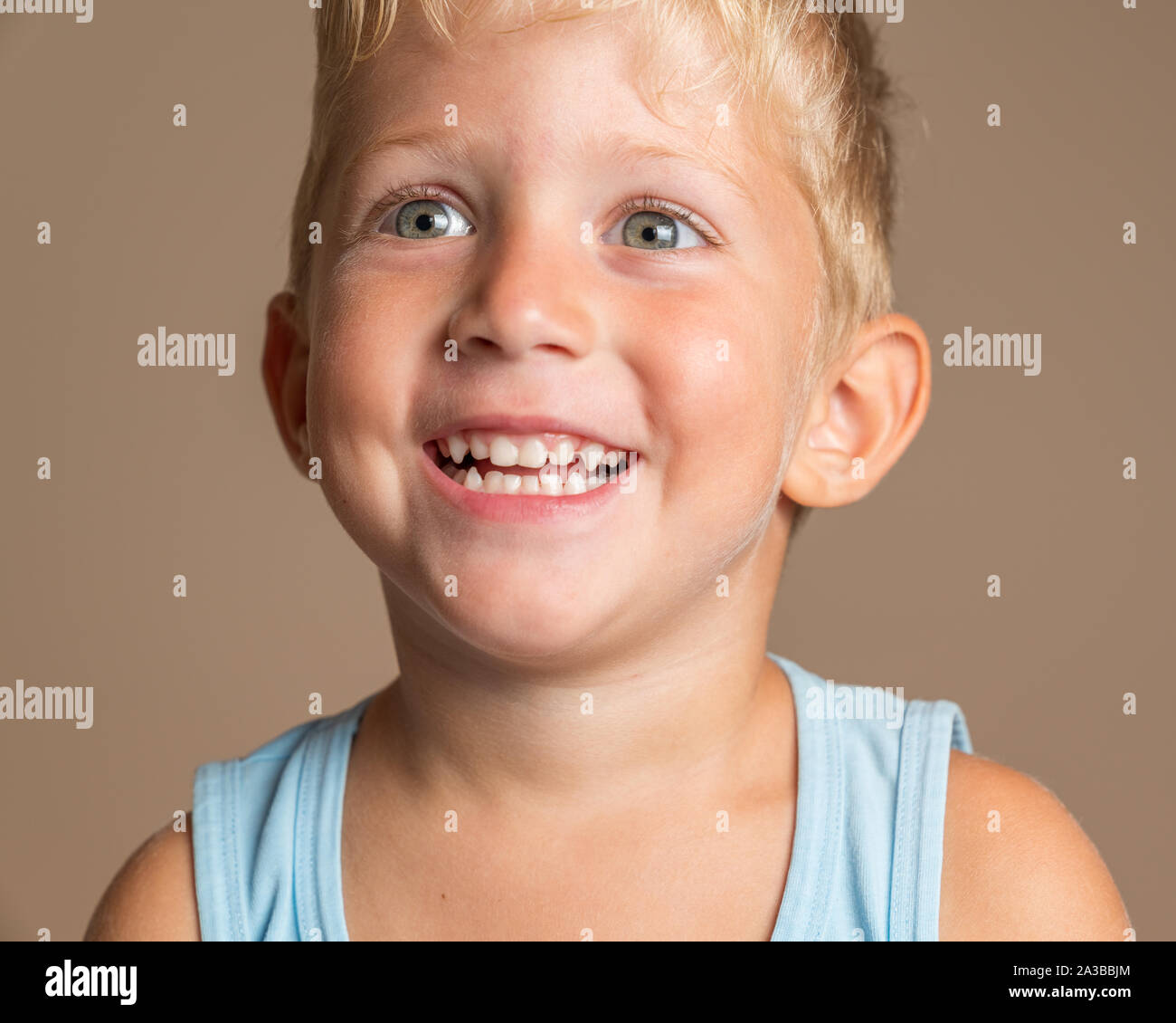 Closeup of Baby boy smiling three year old, blond with green eyes on a light brown background, conceptual photo for dental hygiene and personal care. Stock Photo