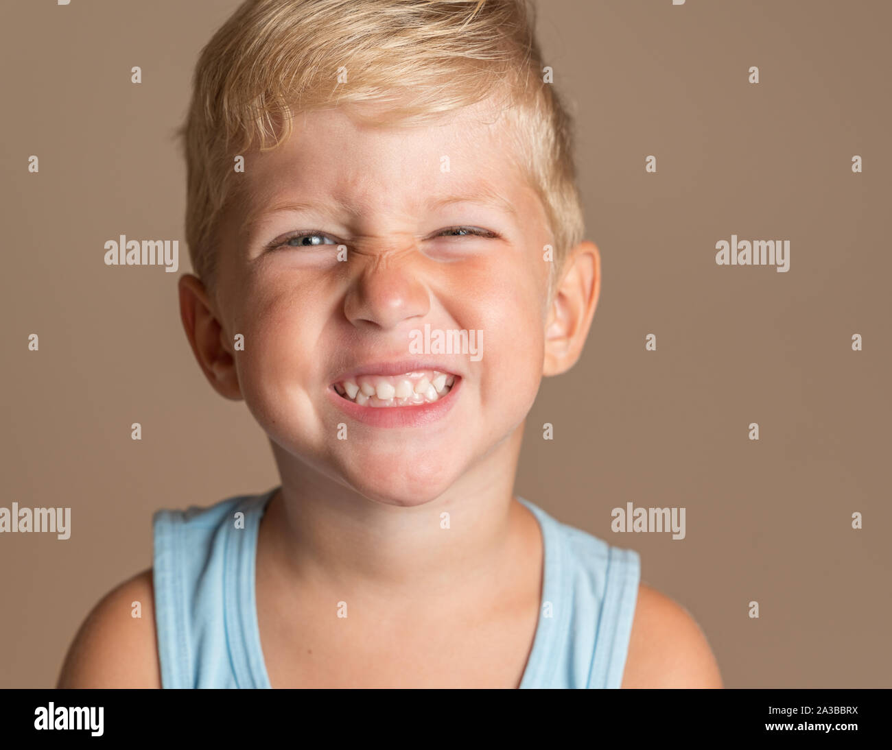 Closeup of Baby boy smiling three year old, blond with green eyes on a light brown background, conceptual photo for dental hygiene and personal care. Stock Photo