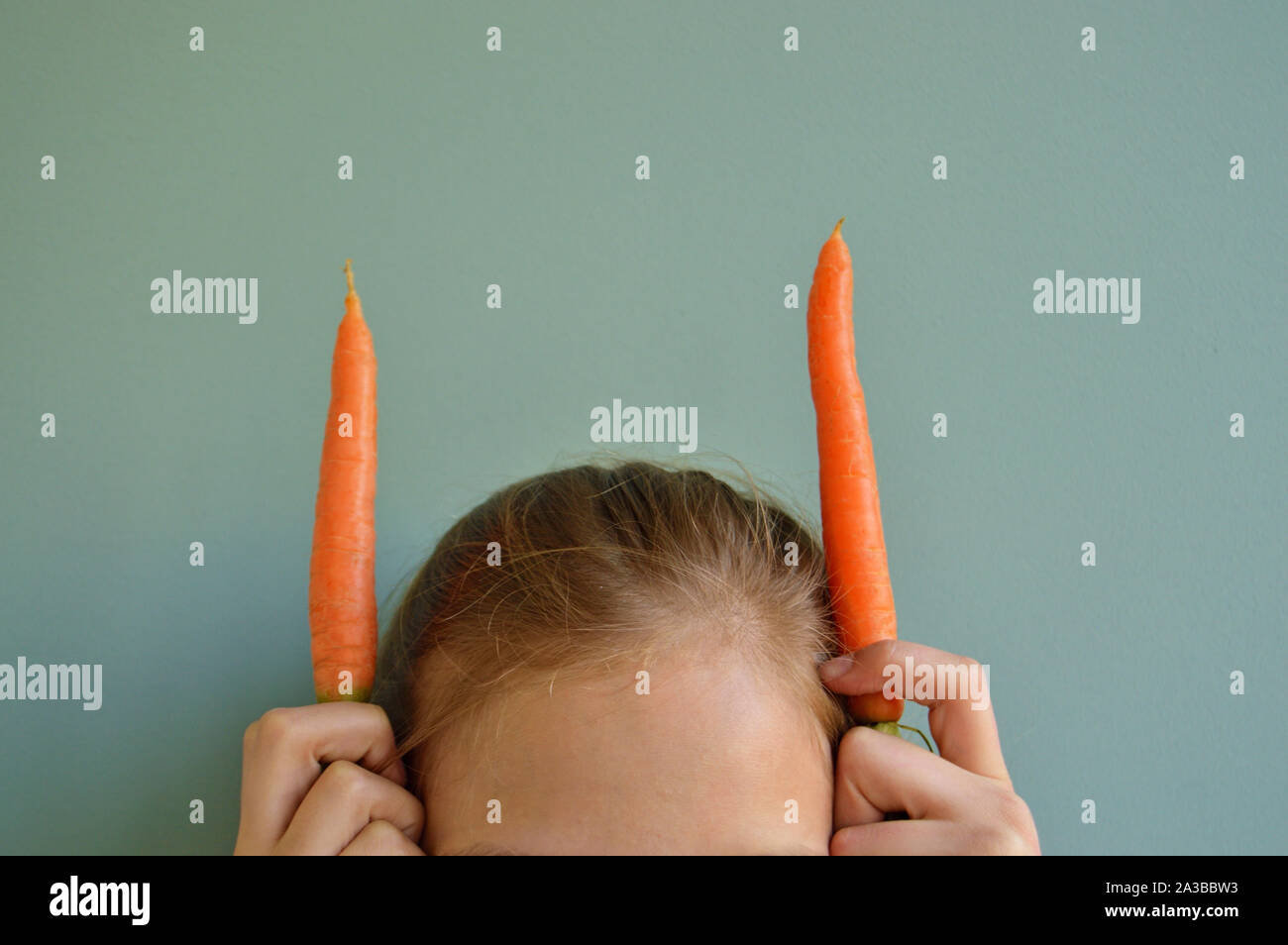 Girl holding two carrots next to head Stock Photo