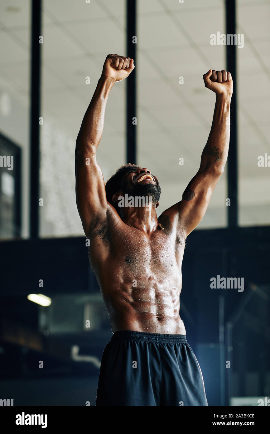Happy fit man with defined abdominal muscules laughing and rising arms ...