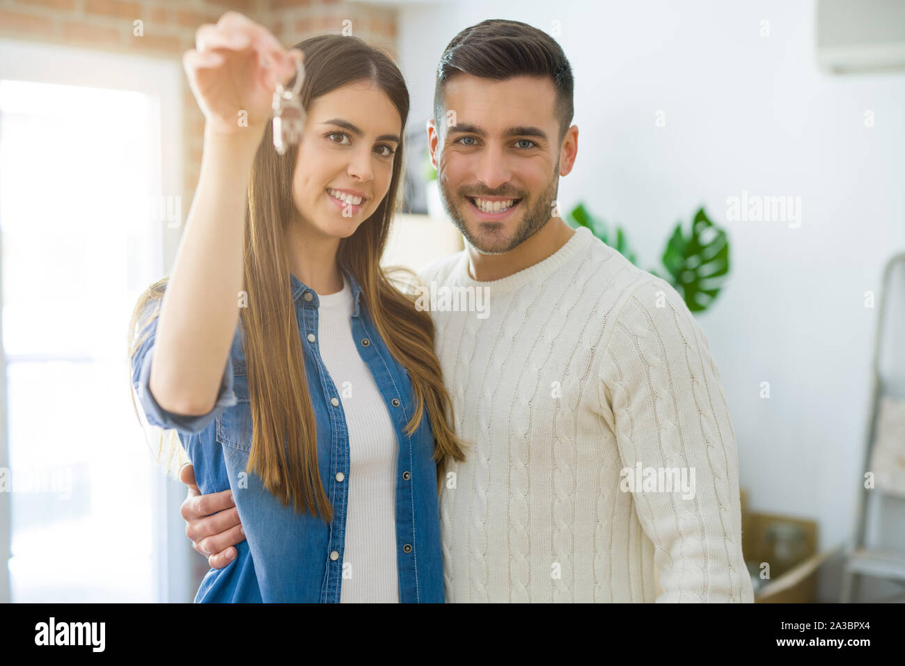Young couple moving to a new home, hugging in love showing keys of new ...