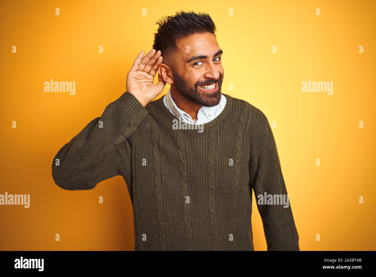 Young indian man wearing green sweater and shirt standing over isolated ...