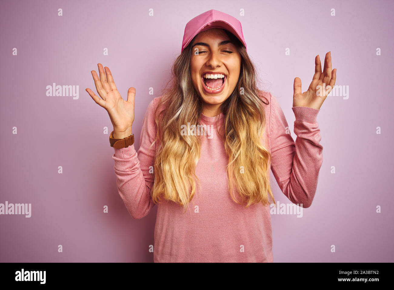 Young beautiful woman wearing cap over pink isolated background celebrating mad and crazy for success with arms raised and closed eyes screaming excit Stock Photo