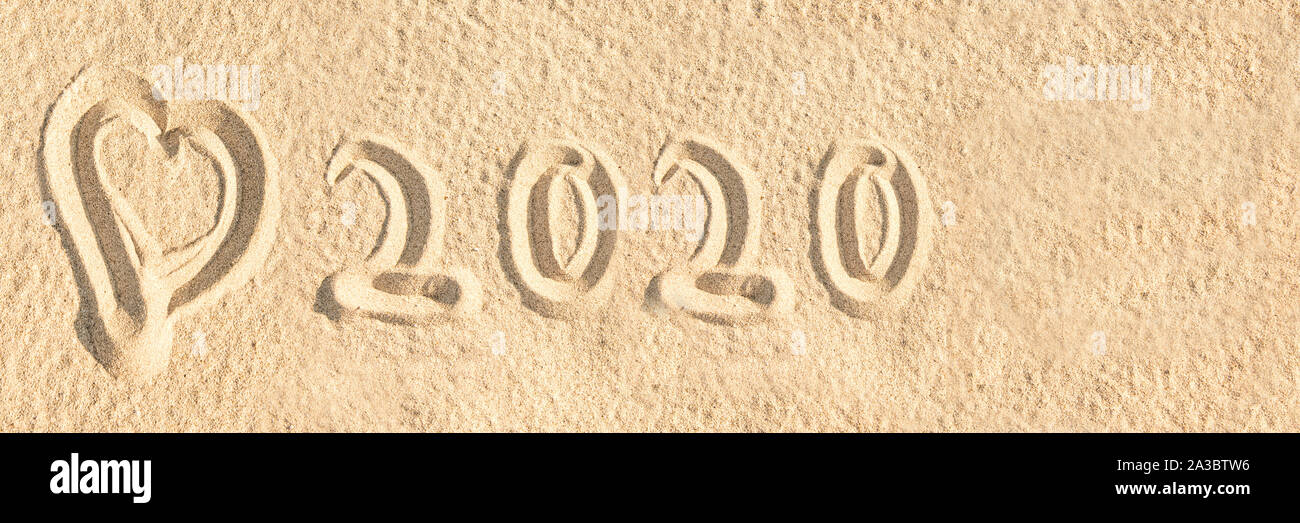 Year 2020 written in the sand of a beach with a heart, travel panoramic banner Stock Photo