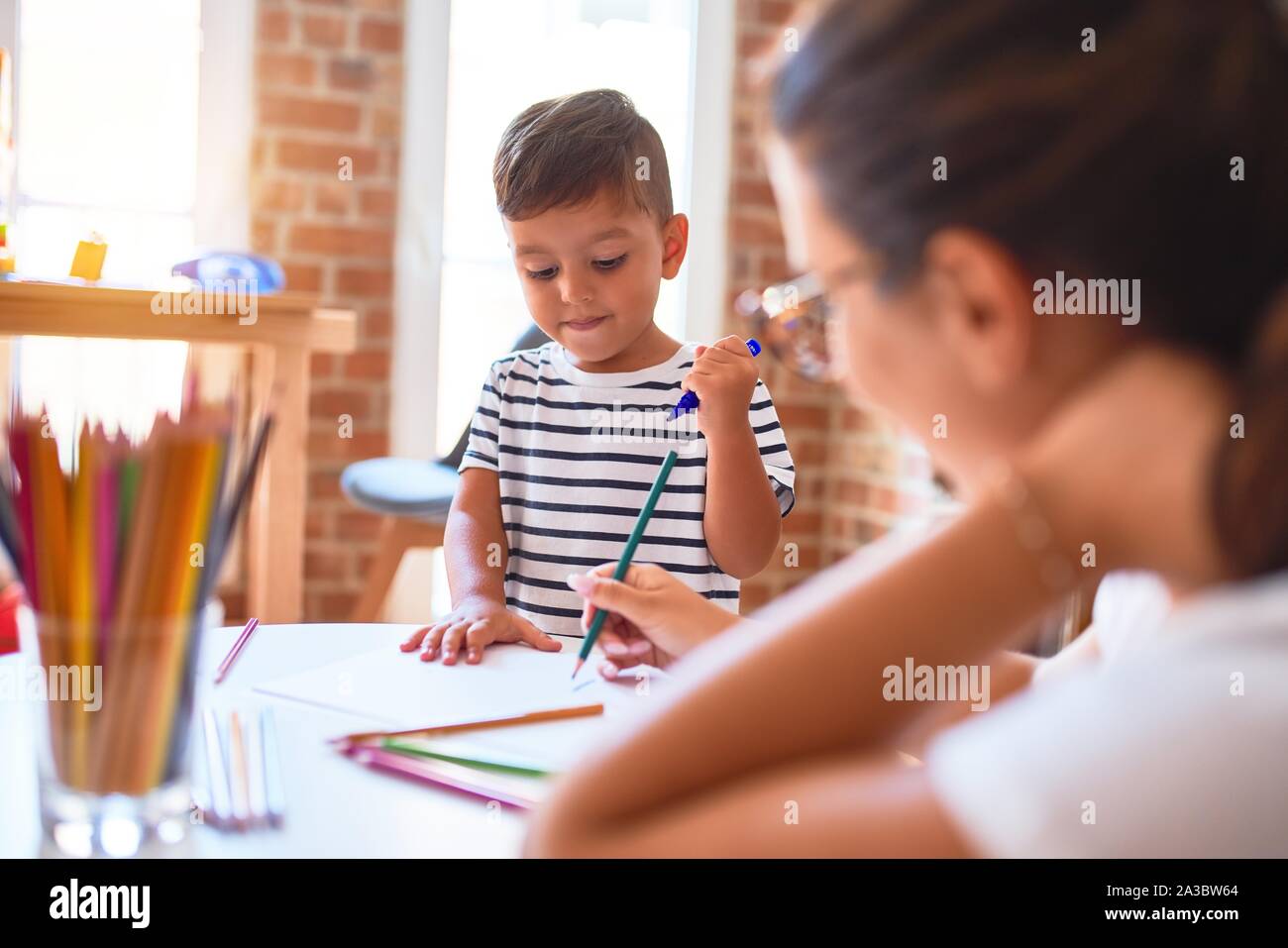 Beautiful teacher and toddler boy drawing draw using colored pencils at ...