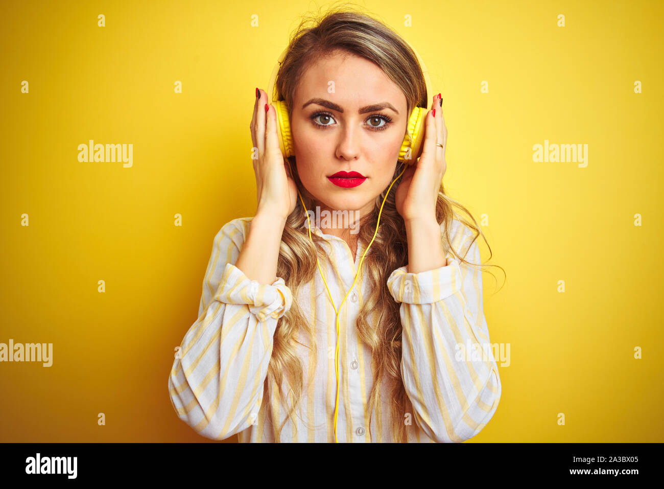 Young beautiful woman listening to music using headphones over yellow ...
