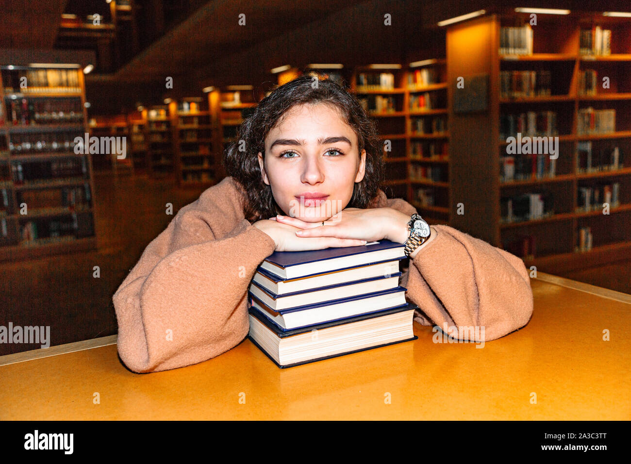 Young woman holding stack of books in library Stock Photo - Alamy