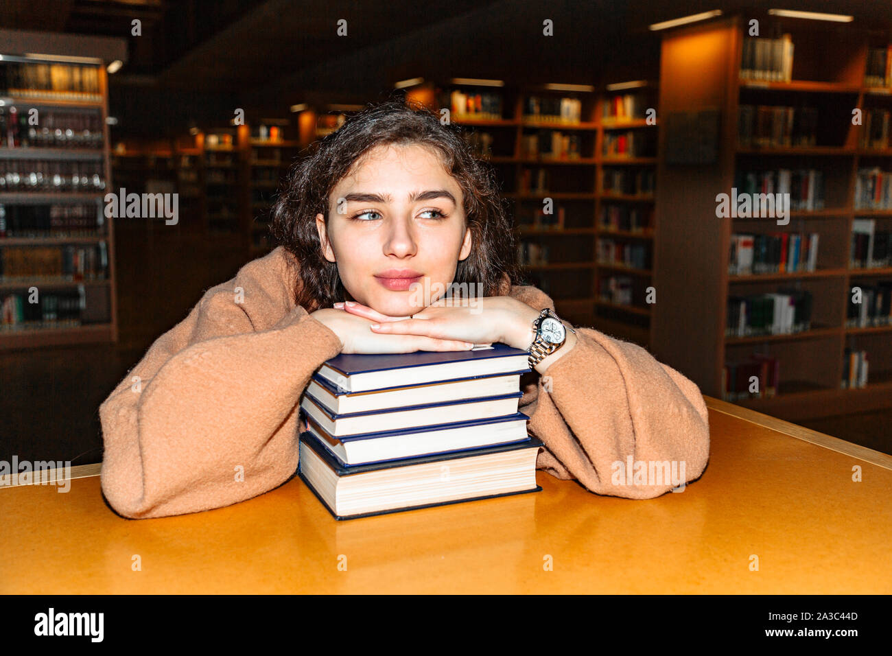 Young woman holding stack of books in library Stock Photo - Alamy