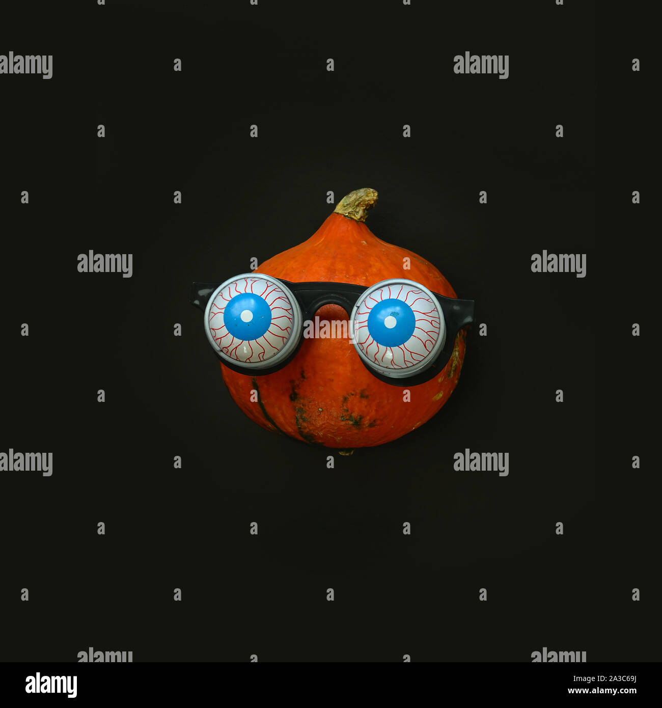 Flat lay Halloween background with nice pumpkin in in glasses horror symbol eyeball on black backdrop. Festive concept. Stock Photo