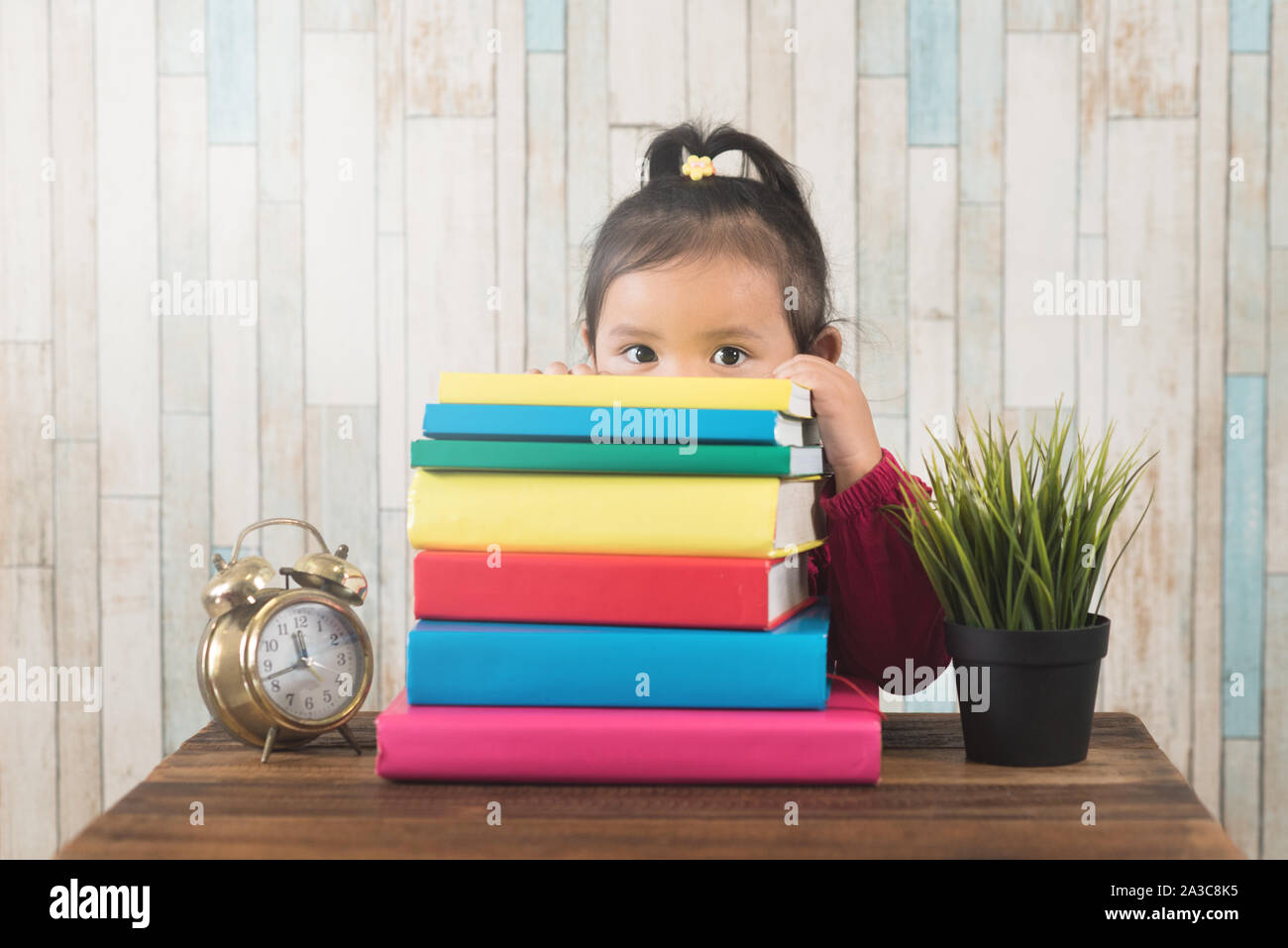 cute little asian girl peeping from behind stack of books. Concept of education, couriousity and child growth development Stock Photo