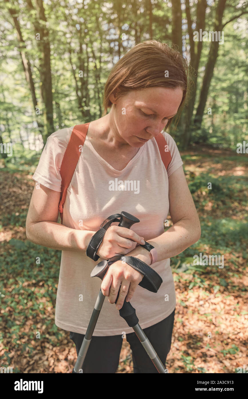 Female hiker checking smart fitness bracelet while trekking through forest Stock Photo