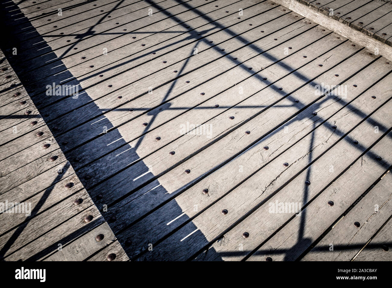 a weathered wooden bridge or decking with the shadow of the railing creating a constrasting pattern on the wood. Stock Photo