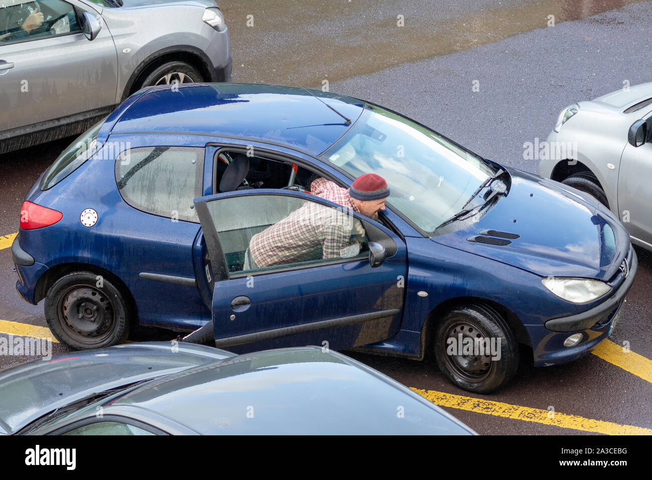 Miserable weather lone single man struggling pushing a broke down car on car park in Killarney, County Kerry, Ireland Stock Photo