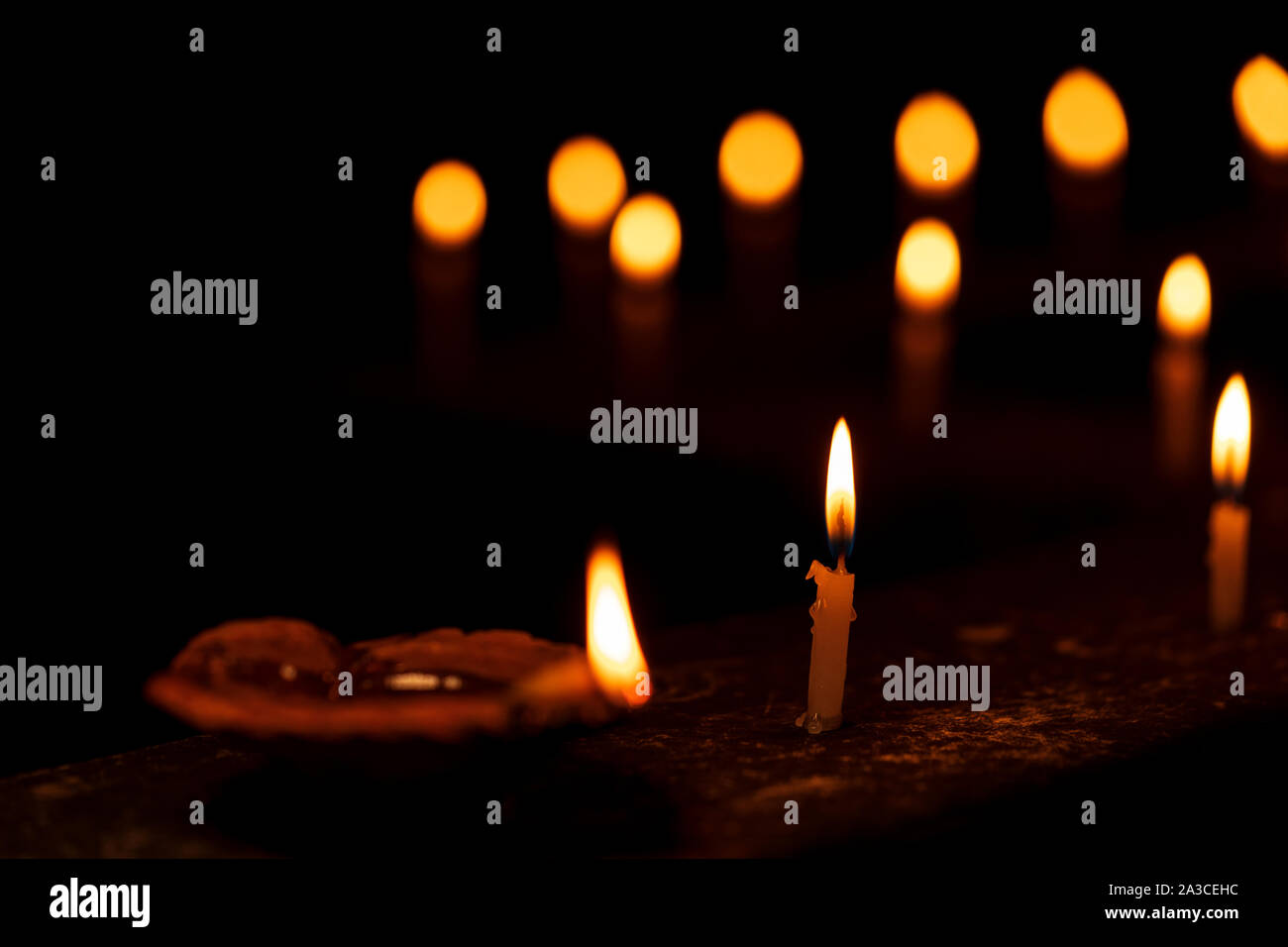 A row of traditional earthen lamps or diya and candles burning during Diwali Festive celebrations. Background concept for temple,worship, faith, belie Stock Photo