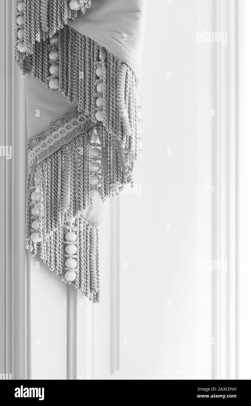 Decorative white luxury curtains with fringe over white wall. Closeup