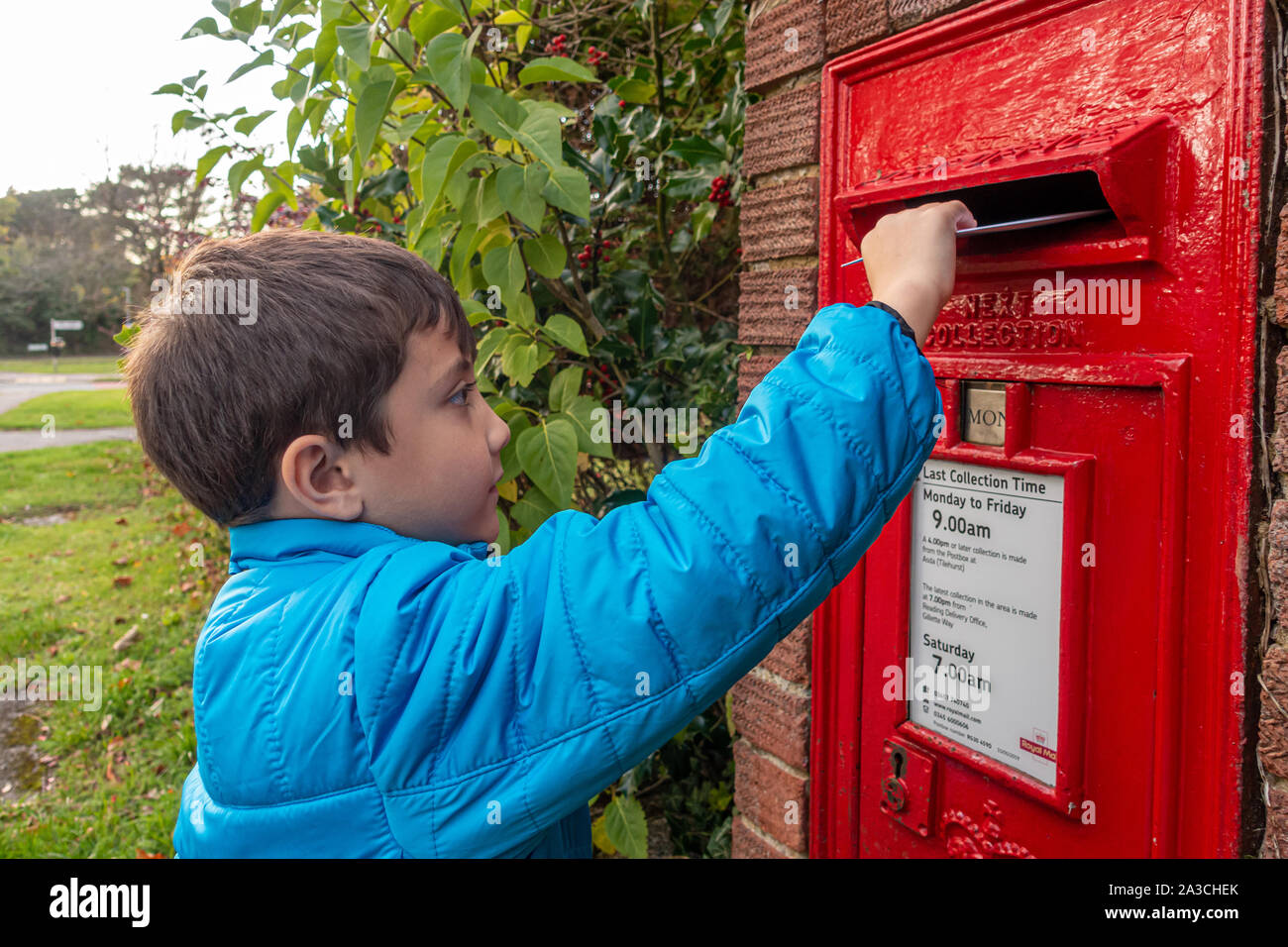 A young boy posts a letter in a post box built into a wall. Stock Photo